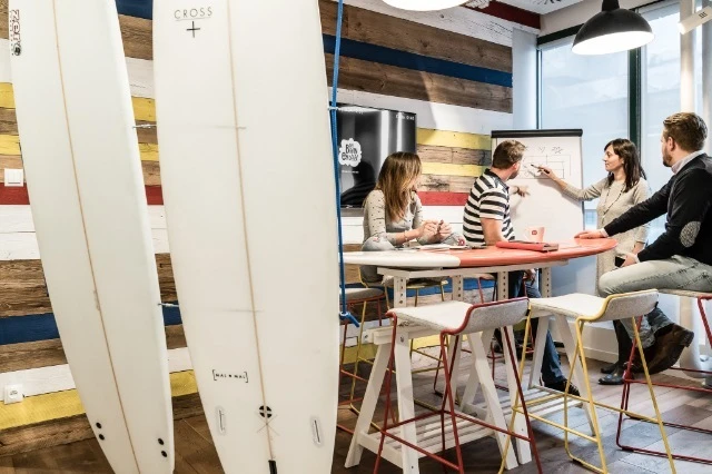 Spotkanie zespołu w kreatywnej przestrzeni biurowej z deskami surfingowymi i planszą do prezentacji