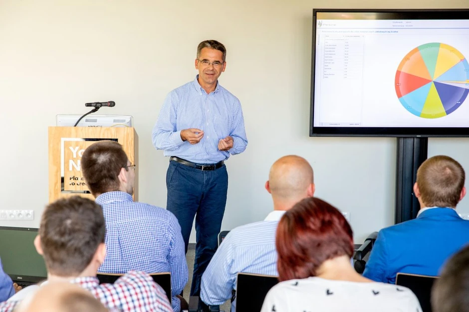 Mężczyzna prowadzi prezentację biznesową przed grupą uczestników w nowoczesnej sali konferencyjnej