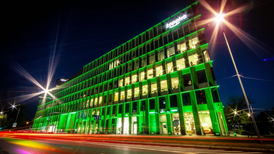 Nowoczesny, oświetlony zielonym światłem biurowiec firmy Żabka nocą w dynamicznym ujęciu ulicy przed budynkiem