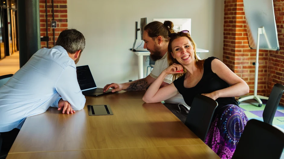 Trójka pracowników omawia projekt przy stole w nowoczesnym biurze z ceglaną ścianą w tle