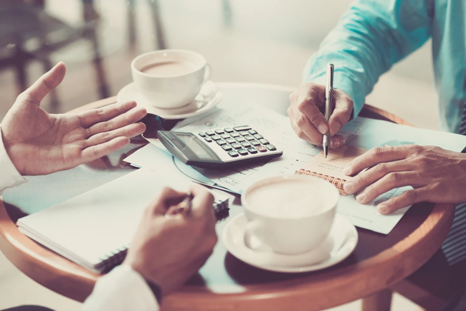 Dwie osoby omawiają dokumenty i notują przy kawie z kalkulatorem na drewnianym stole