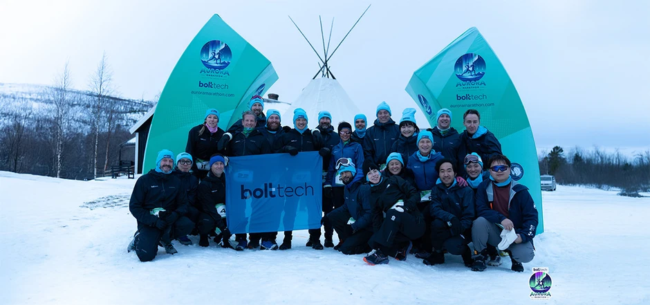 Zespół bolttec na zimowym biegu Aurora Marathon pozujący razem przy namiocie tipi na śniegu