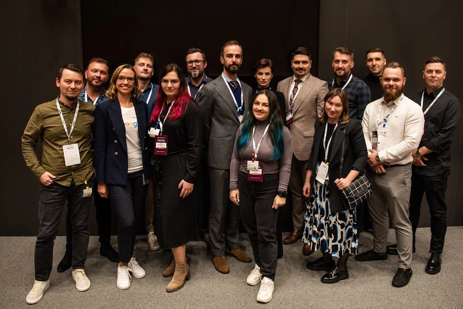 Grupa zawodowo ubranych osób pozujących razem na tle ciemnej ściany podczas wydarzenia firmowego