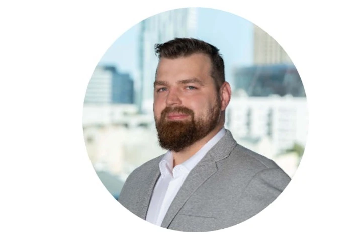 Portret mężczyzny z brodą w jasnej marynarce z widokiem biurowców w tle