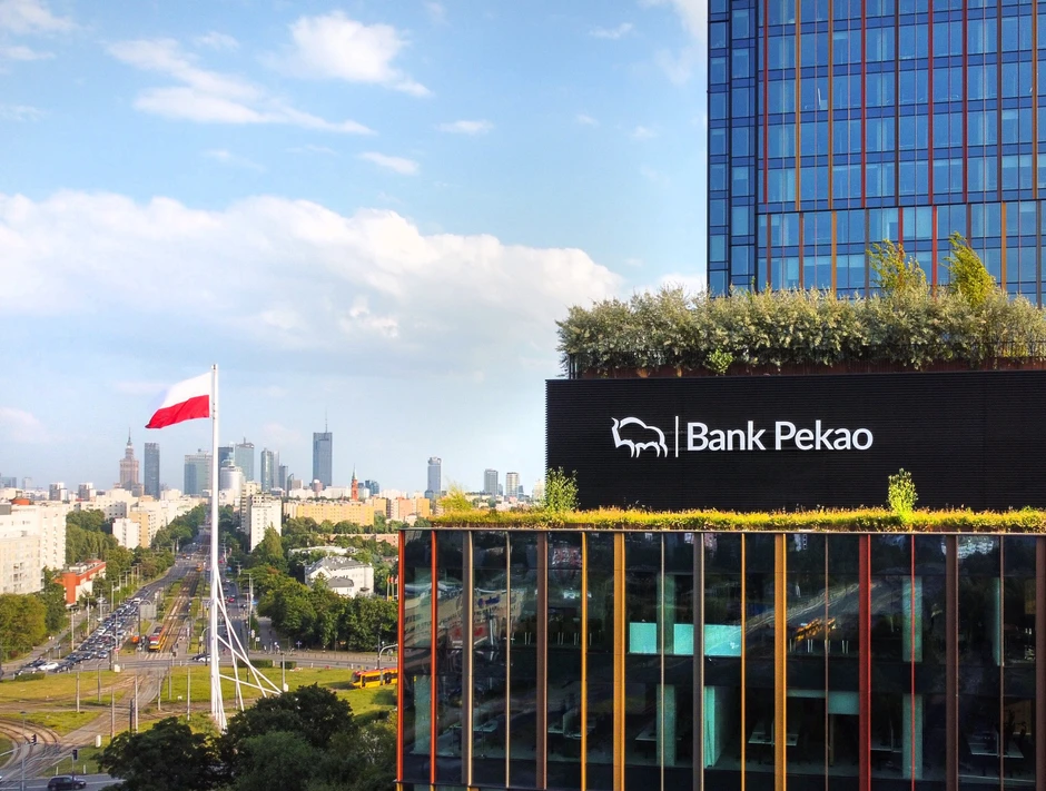 Nowoczesny budynek Banku Pekao z zielonym dachem na tle panoramy Warszawy i polską flagą