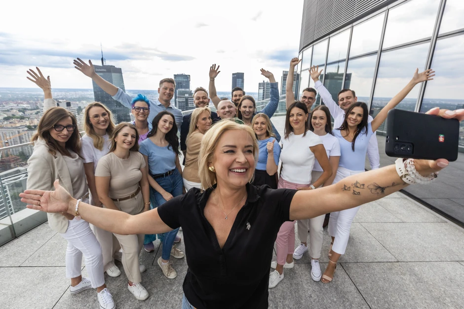 Grupa uśmiechniętych pracowników robi wspólne zdjęcie na tarasie nowoczesnego biurowca w mieście