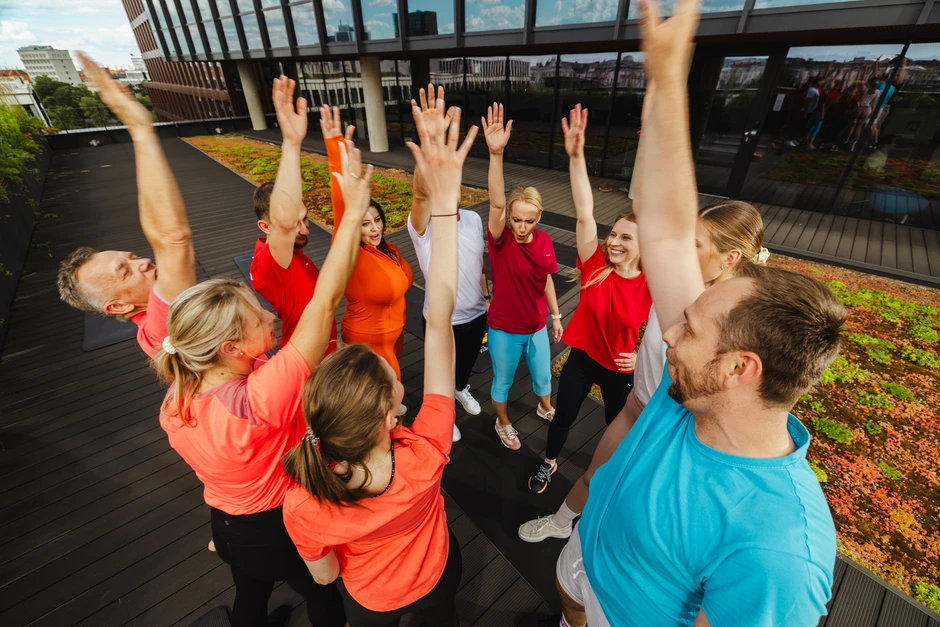 Grupa pracowników na tarasie biurowca podczas integracyjnej aktywności z podniesionymi rękami