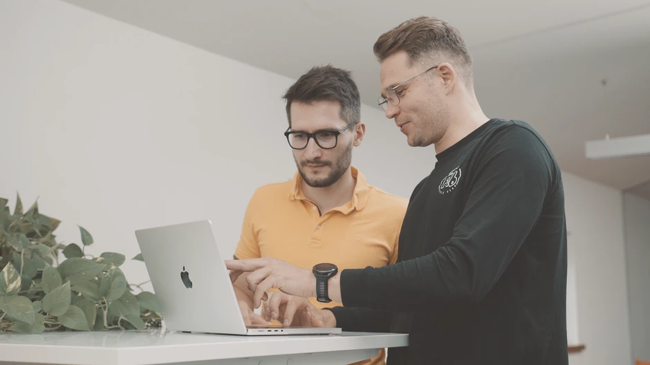 Dwóch mężczyzn pracuje razem przy laptopie w nowoczesnym biurze z roślinami w tle