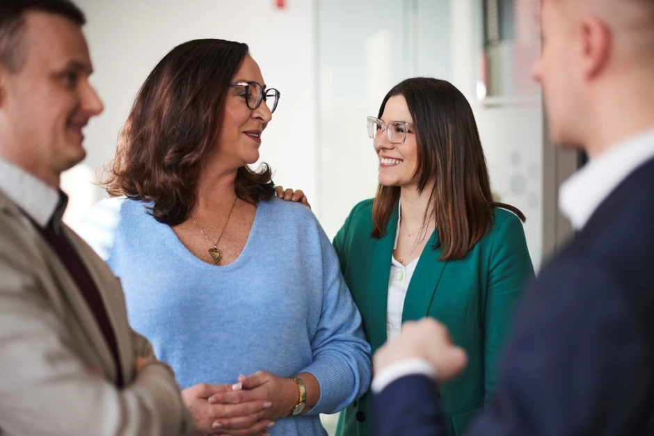 Grupa czterech osób rozmawia i uśmiecha się w nowoczesnym biurze, budując pozytywną atmosferę