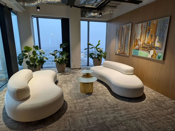 Nowoczesne wnętrze biura z białymi kanapami, złotymi stolikami i roślinami przy dużych oknach