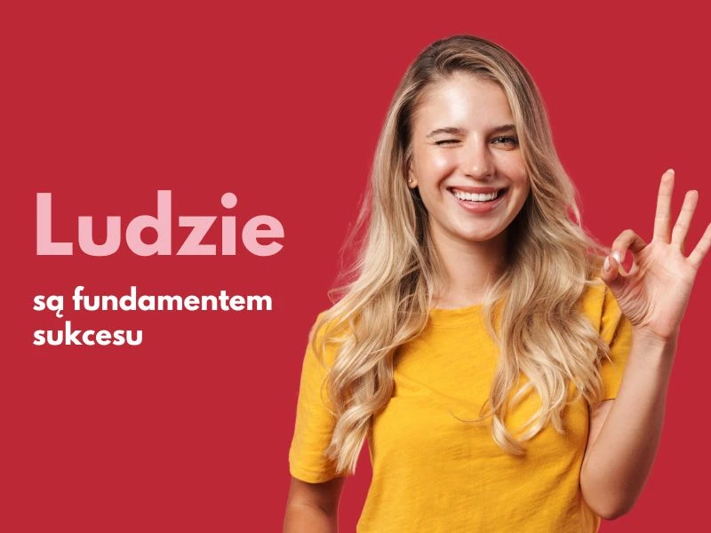 Uśmiechnięta młoda kobieta w żółtej bluzce robi gest OK na czerwonym tle z napisem Ludzie są fundamentem sukcesu