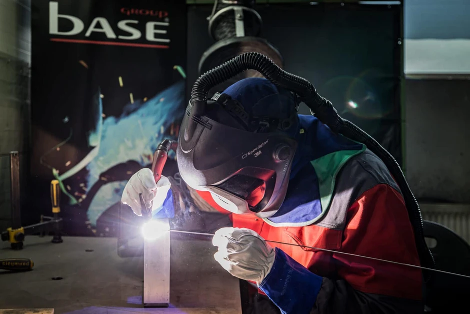 Pracownik w kombinezonie i hełmie spawalniczym precyzyjnie wykonuje spawanie metalu w warsztacie