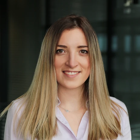 Uśmiechnięta młoda kobieta w jasnej koszuli na tle biurowego wnętrza firmy