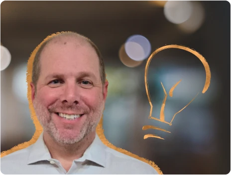 Uśmiechnięty mężczyzna w koszuli na tle rozmytego biura i ikony żarówki symbolizującej kreatywność