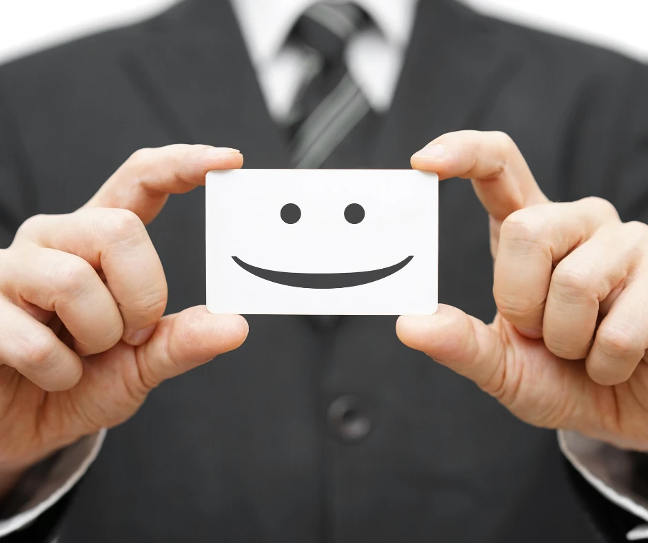 Biznesmen w garniturze trzyma kartę z uśmiechniętą emotikoną symbolizującą pozytywne nastawienie i obsługę