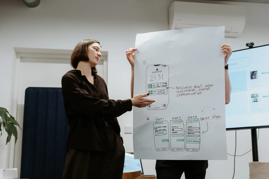 Kobieta prezentuje projekt aplikacji na dużym papierze podczas spotkania w biurze firmy