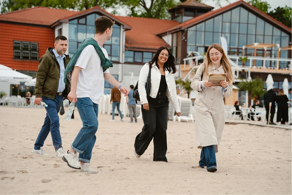 Grupa pracowników spaceruje i rozmawia na plaży przed nowoczesnym biurem z dużymi oknami