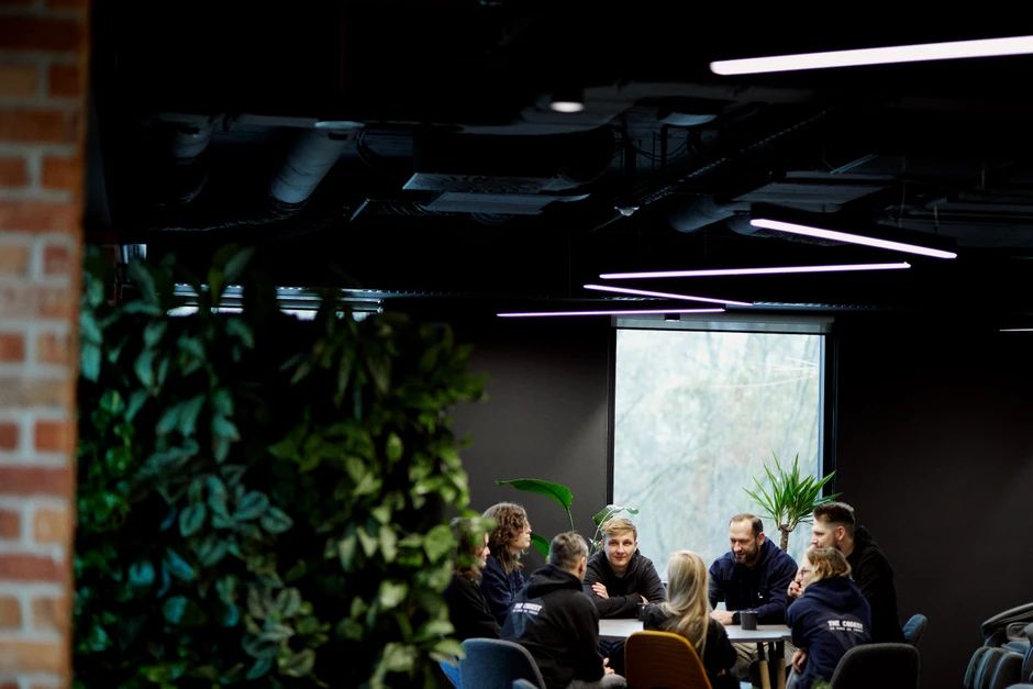 Zespół pracowników omawia projekt przy stole w nowoczesnym biurze z dużym oknem i roślinami