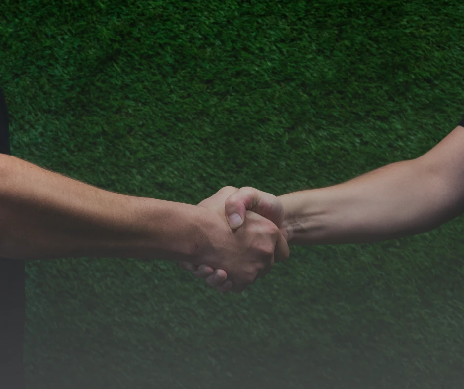 Uścisk dłoni dwóch osób na tle zielonej trawy symbolizujący współpracę i zaufanie