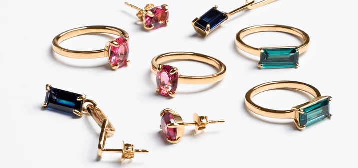 Złote pierścionki i kolczyki z różnokolorowymi szlachetnymi kamieniami na białym tle