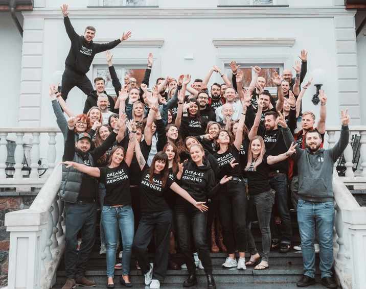 Zespół firmy na zdjęciu grupowym na schodach przed budynkiem ubrany w czarne bluzy i koszulki z napisem Dreams Into Memories