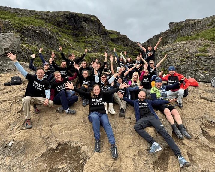 Grupa pracowników na wycieczce integracyjnej siedzi na kamieniach w krajobrazie skalnym z rękami w górze