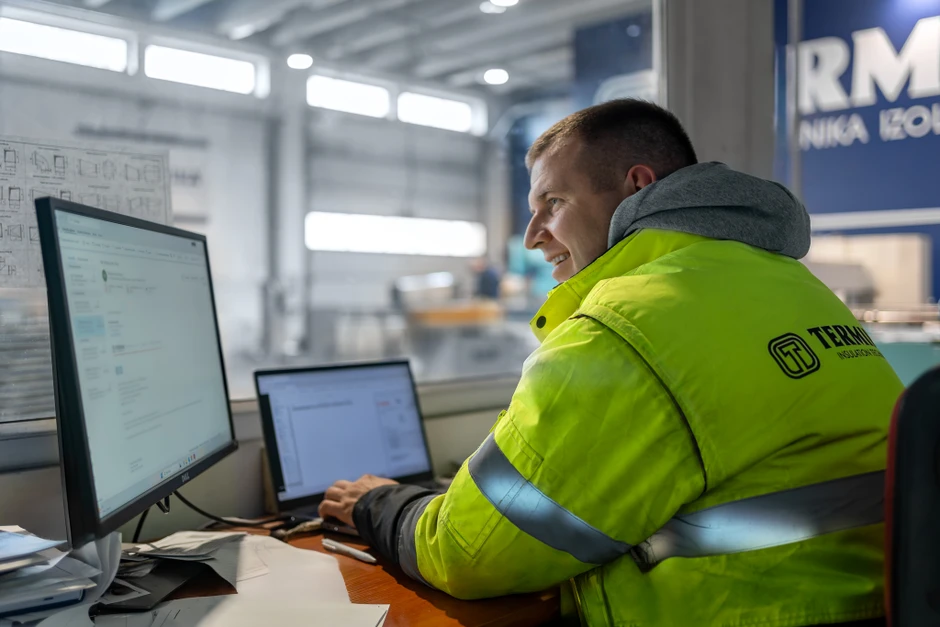 Pracownik w odblaskowej kurtce korzysta z komputera w nowoczesnym biurze firmy Termika Izolacje