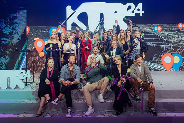 Grupa pracowników firmy na scenie z kolorowymi rekwizytami podczas firmowego wydarzenia pod logo KM24