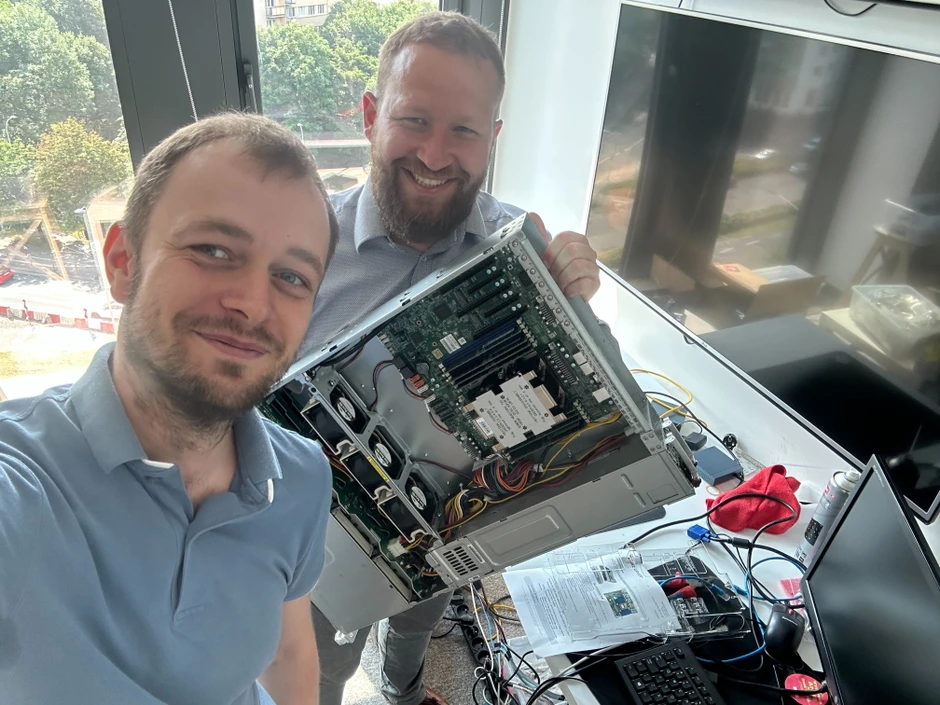 Dwóch mężczyzn naprawia komputer w nowoczesnym biurze z dużymi oknami i sprzętem biurowym