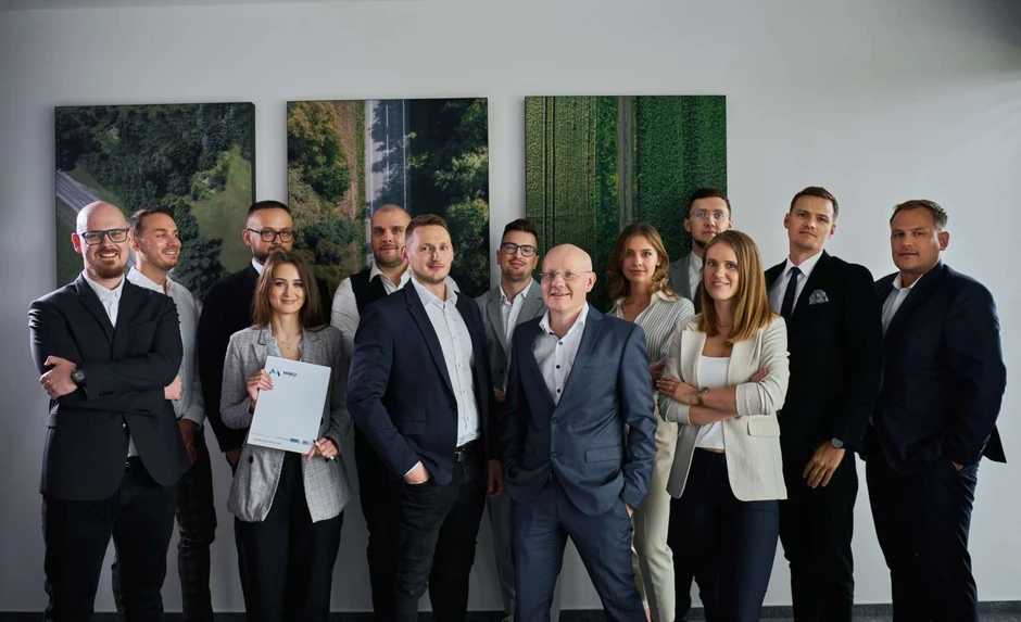 Zespół profesjonalistów w formalnych stylizacjach pozuje na tle nowoczesnej galerii zdjęć lotniczych