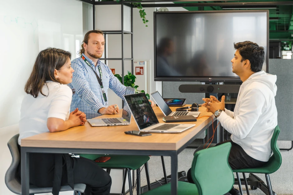 Trzy osoby prowadzą kreatywne spotkanie zespołowe przy stole z laptopami w nowoczesnym biurze