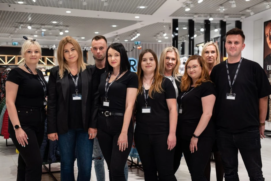 Zespół dziesięciu pracowników w czarnych strojach stoi razem w nowoczesnym sklepie z odzieżą