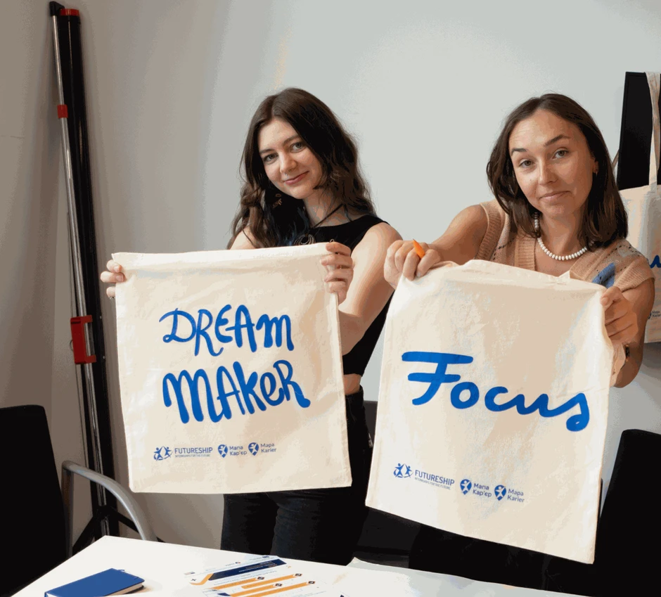 Dwie uśmiechnięte kobiety prezentują torby z napisami dream maker i focus podczas wydarzenia firmowego