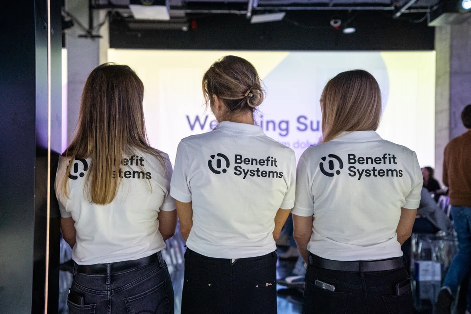 Trzy osoby w koszulkach Benefit Systems podczas wewnętrznego eventu firmowego w nowoczesnym biurze