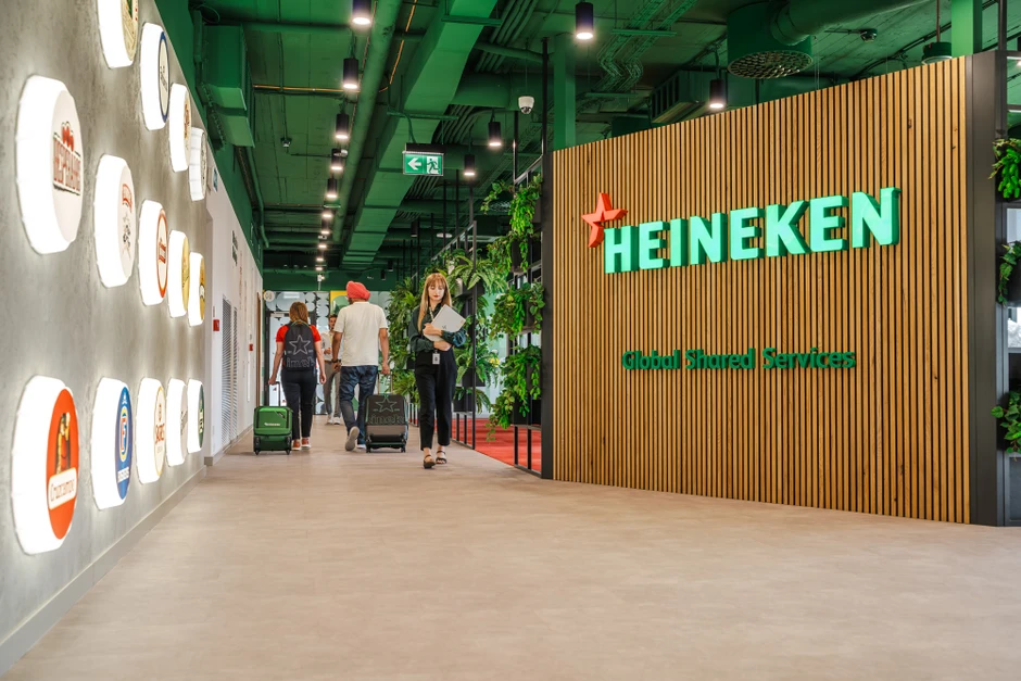 Nowoczesne biuro Heineken z zielonym sufitem, drewnianą ścianą i pracownikami w korytarzu