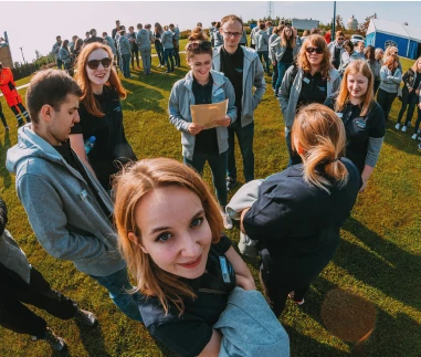 Zespół młodych pracowników spotyka się na zewnątrz podczas firmowego wydarzenia integracyjnego na trawie