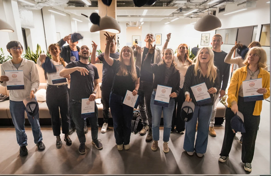 Grupa pracowników świętuje sukces, trzymając dyplomy i rzucając czapki w nowoczesnym biurze