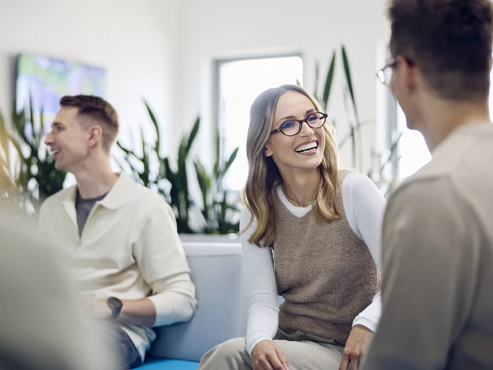 Grupa młodych pracowników rozmawia i śmieje się podczas spotkania w jasnym biurze z roślinami