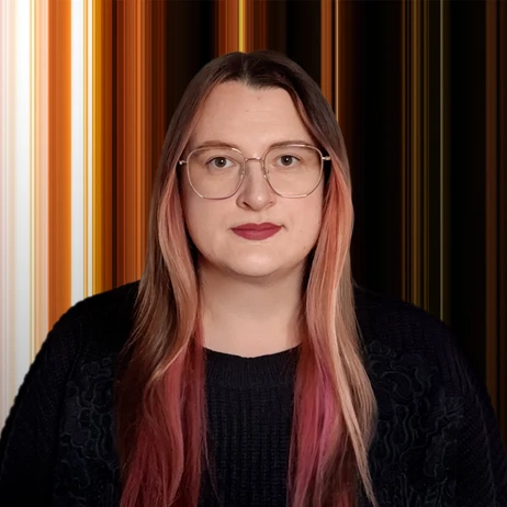 Portret osoby z długimi różowymi włosami, w okularach i ciemnym swetrze na abstrakcyjnym tle