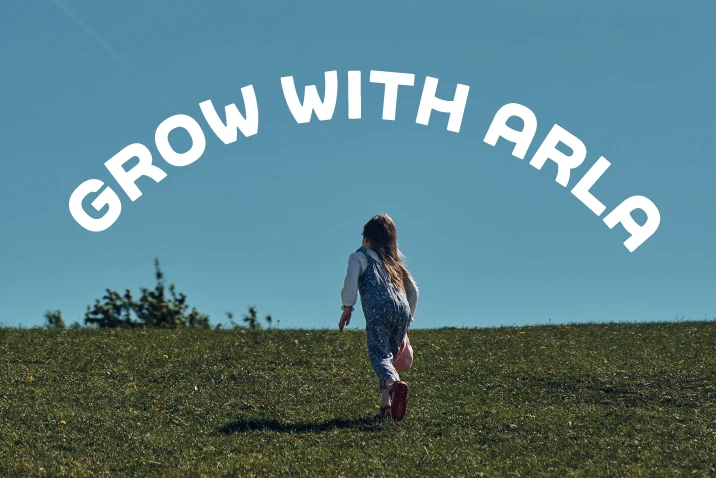 Dziecko biega po zielonym wzgórzu pod błękitnym niebem z napisem Grow with Arla