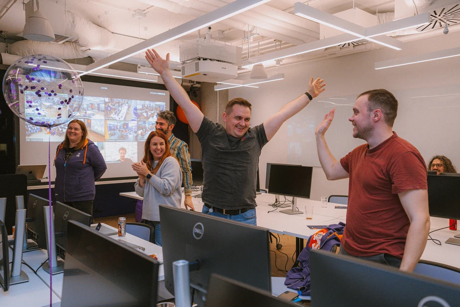 Zespół pracowników świętuje sukces w nowoczesnym biurze przy komputerach i balonie