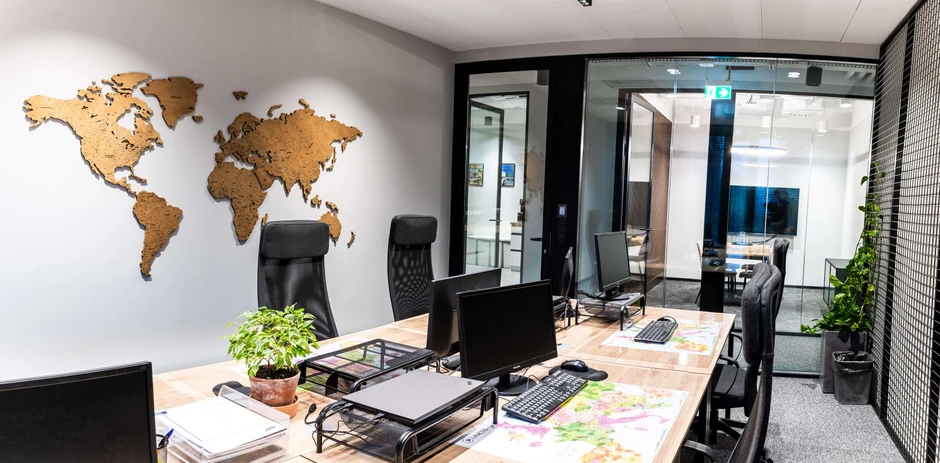 Nowoczesne biuro z drewnianą mapą świata na ścianie oraz stanowiskami pracy z komputerami i roślinami