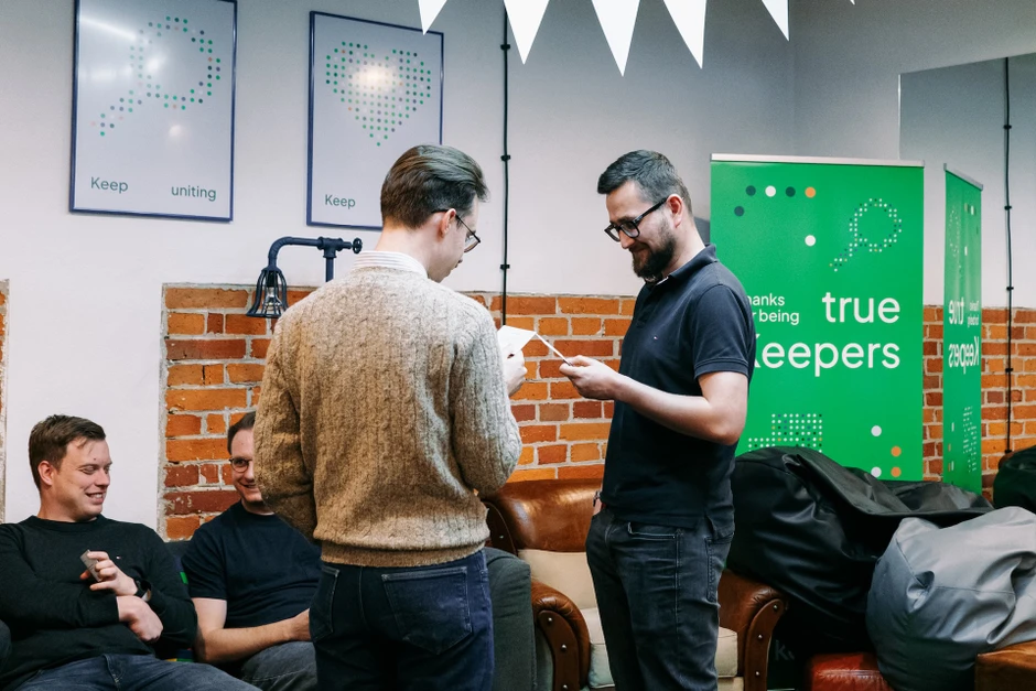 Dwóch mężczyzn rozmawia i czyta kartki w przyjaznym biurowym wnętrzu z ceglanymi ścianami