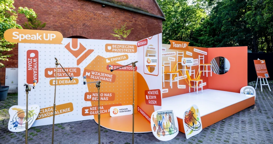 Kolorowa scena eventowa z mikrofonami i hasłami promującymi otwartość i współpracę w firmie