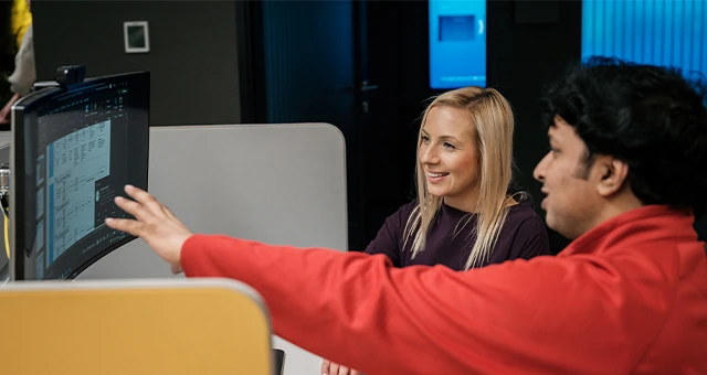 Dwójka pracowników omawia projekt przy monitorze w nowoczesnym biurze pełnym energii i współpracy