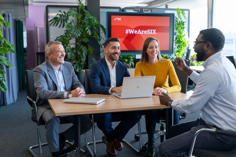 Czterech uśmiechniętych pracowników prowadzi spotkanie biznesowe w nowoczesnym biurze przy laptopach