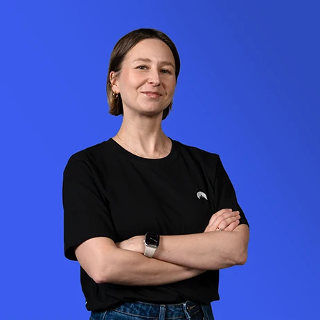 Młoda kobieta uśmiechnięta z założonymi rękami na tle niebieskiego tła w casualowym stroju