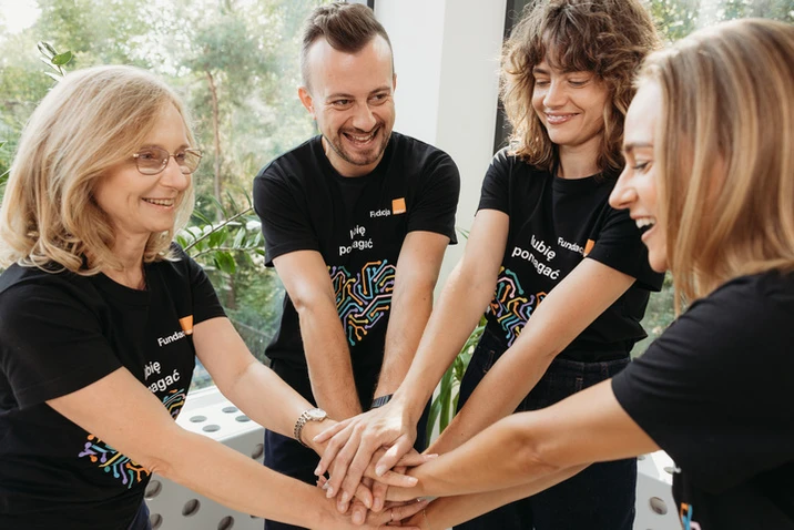 Cztery osoby w koszulkach zespołowych łączą ręce w geście współpracy i wsparcia