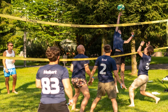 Zespół młodych mężczyzn grających w siatkówkę plażową na zielonym boisku podczas słonecznego dnia
