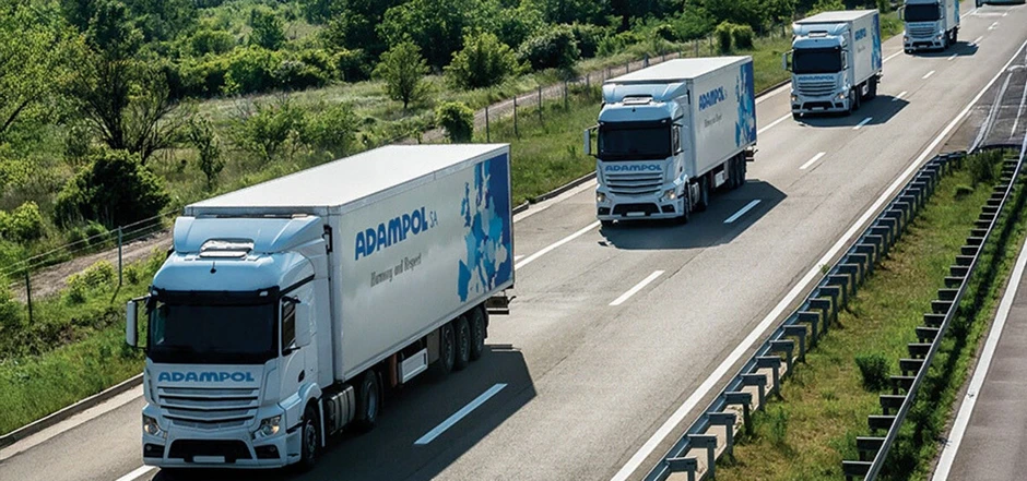 Flota nowoczesnych ciężarówek Adampol na drodze w otoczeniu zieleni, symbol profesjonalnego transportu